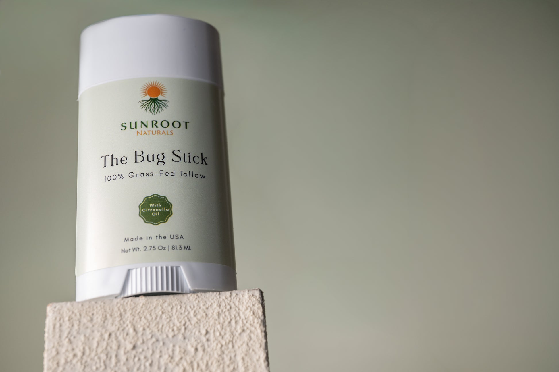 Sunroot The Bug Stick insect repellent displayed on textured pedestal against neutral background.