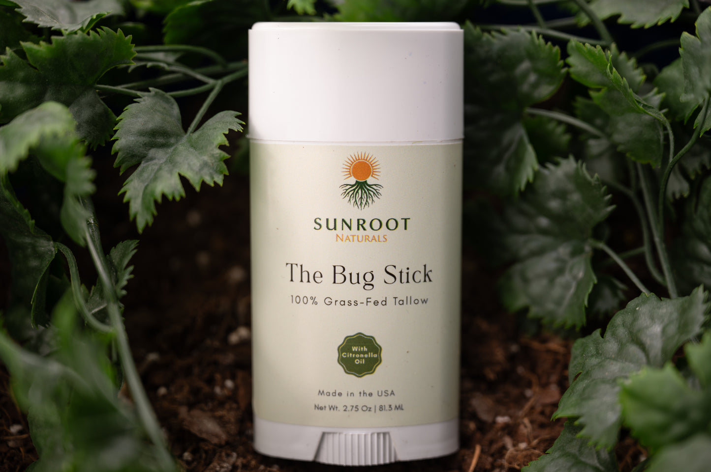 Sunroot The Bug Stick insect repellent displayed outdoors among green foliage and natural ground cover.
